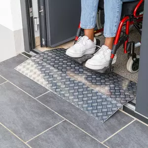 Eine Person im Rollstuhl benutzt eine Schwellenbrücke