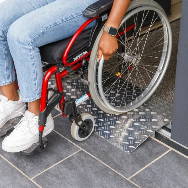 Eine Person im Rollstuhl benutzt eine Schwellenbrücke aus Aluminium