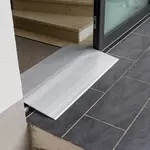 Eine hohe Schwellenbrücke aus Aluminium überbrückt eine Türschwelle zwischen einer Innentreppe und einer gefliesten Außenfläche.