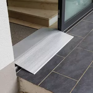Eine hohe Schwellenbrücke aus Aluminium überbrückt eine Türschwelle zwischen einer Innentreppe und einer gefliesten Außenfläche.