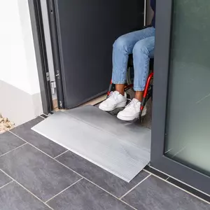 Eine Person im Rollstuhl benutzt eine Schwellenbrücke