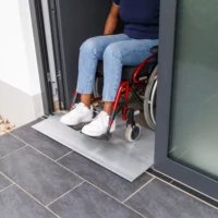 Eine Person im Rollstuhl verlässt ein Gebäude über eine Schwellenbrücke