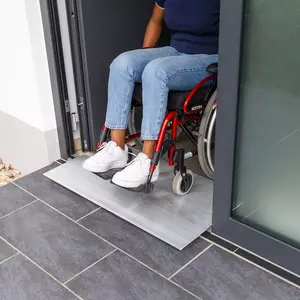 Eine Person im Rollstuhl verlässt ein Gebäude über eine Schwellenbrücke