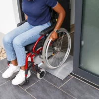 Eine Person im Rollstuhl benutzt eine Schwellenbrücke