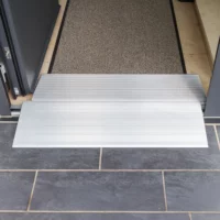 Zwei Schwellenbrücken aus Alumimium für Rollstühle an einem Türeingang mit dunklem Fliesenboden und einer strukturierten Matte im Inneren.