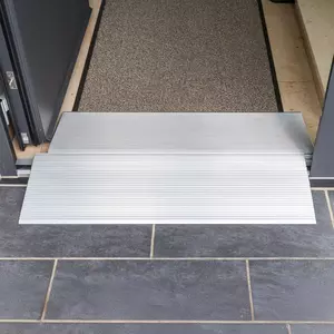 Zwei Schwellenbrücken aus Alumimium  für Rollstühle an einem Türeingang mit dunklem Fliesenboden und einer strukturierten Matte im Inneren.