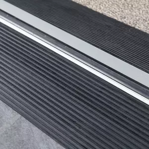 Nahaufnahme der Oberfläche zweier schwarzer Schwellenkeile mit Rillen neben einer Türkante und einem Teppichboden.