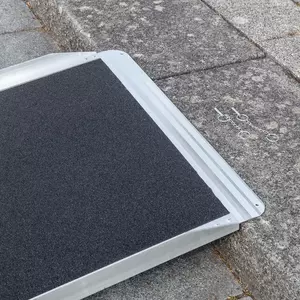 Nahaufnahme der oberen Auflagefläche einer Rollstuhlrampe mit strukturierter schwarzer Oberfläche auf einer grauen Steinstufe.