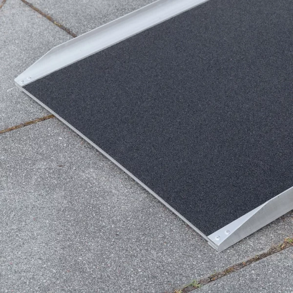 Nahaufnahme der unteren Auflagefläche einer Rollstuhlrampe mit strukturierter schwarzer Oberfläche auf einem grauen Betonpflaster.