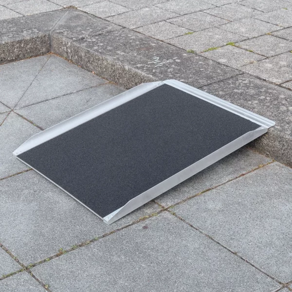 28 Rollstuhlrampe Stufenrampe leicht diagonal rechts Eine tragbare Rollstuhlrampe wird ĂĽber einen Bordstein auf einem gepflasterten Gehweg gelegt.