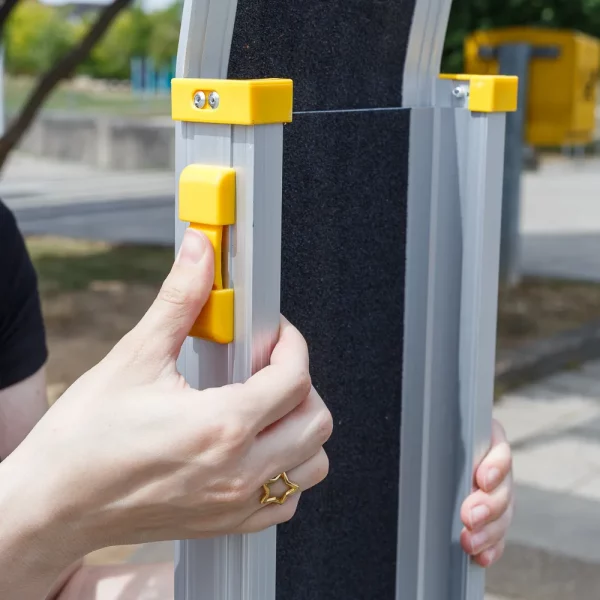 Eine Person drückt die gelbe Verriegelung an einer Rollstuhlrampe aus Aluminium im Freien