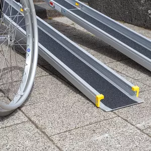 Nahaufnahme der unteren Auflage einer tragbaren Rollstuhlrampe neben einem Rollstuhl