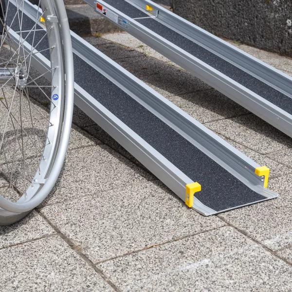 Nahaufnahme der unteren Auflage einer tragbaren Rollstuhlrampe neben einem Rollstuhl