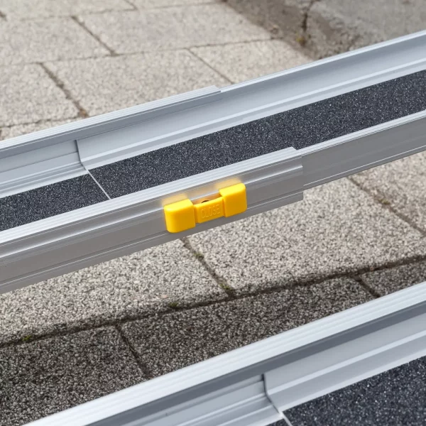 Nahaufnahme der gelben Verriegelung einer aluminiumfarbenen Rollstuhlrampe im Freien