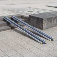 Eine zweiteilige Rollstuhlrampe ist über Steinstufen gelegt und ermöglichen den Zugang von einem niedrigeren zu einem höheren Gehwegniveau.