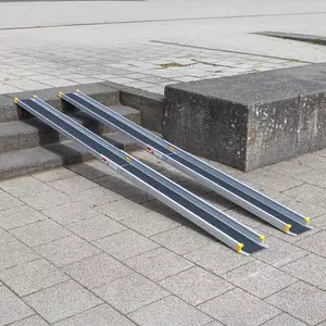 Eine zweiteilige Rollstuhlrampe ist über Steinstufen gelegt und ermöglichen den Zugang von einem niedrigeren zu einem höheren Gehwegniveau.