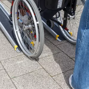 Eine Person im Rollstuhl befährt eine zweiteilige Rollstuhlrampe aus Aluminium während eine Hilfsperson hinter ihr steht.