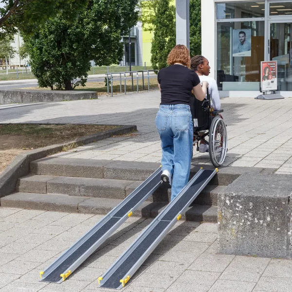 Eine Person schiebt eine andere Person im Rollstuhl auf eine tragbare Rollstuhlrampe