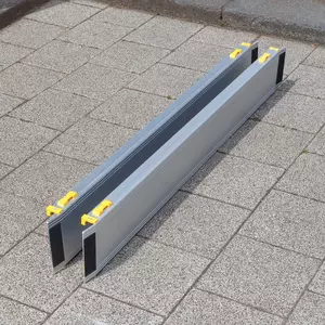 Zwei Rollstuhlrampen aus Aluminium mit gelben Griffen sind zusammengeschoben auf eine gepflasterte Außenfläche gestellt.