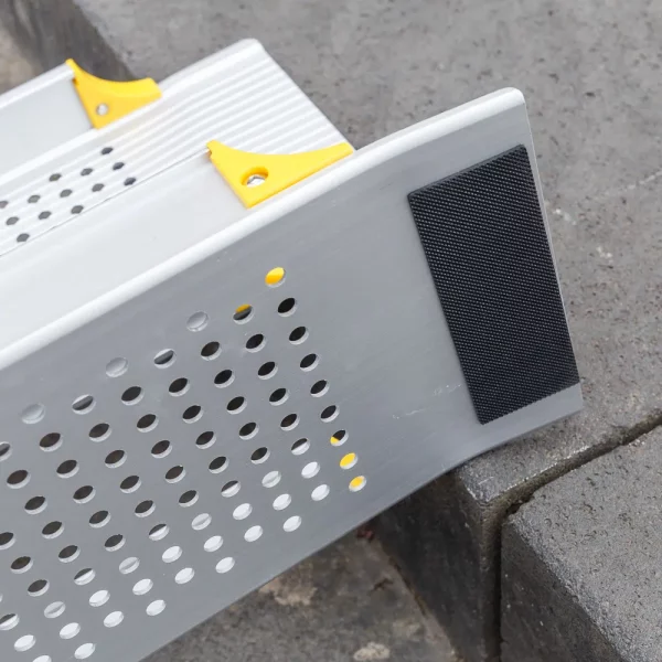Detailaufnahme der Gummierung der oberen Auflage einer Rollstuhlrampe mit gelochter Oberfläche und gelben Akzenten ist auf einer Betonstufe angebracht.