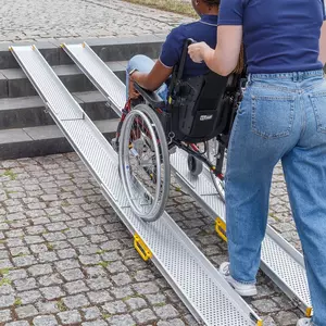 Eine Person schiebt eine andere Person im Rollstuhl über tragbare Schienen