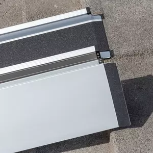 Detailaufnahme der Gummierung der oberen Auflage zweier Rollstuhlrampenschienen die parallel zueinander auf eine Betonfläche aufgestellt sind.