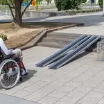 Eine Person im Rollstuhl steht vor zwei Schinene einer tragbaren Rampe