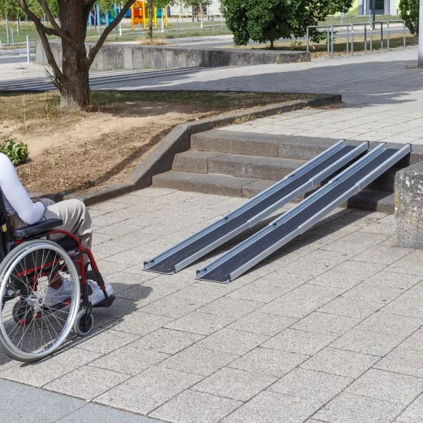 31 Rollstuhlrampe Teleskoprampe breit 3 teilig mit Rollstuhll 1 Eine Person im Rollstuhl steht vor zwei Schinene einer tragbaren Rampe
